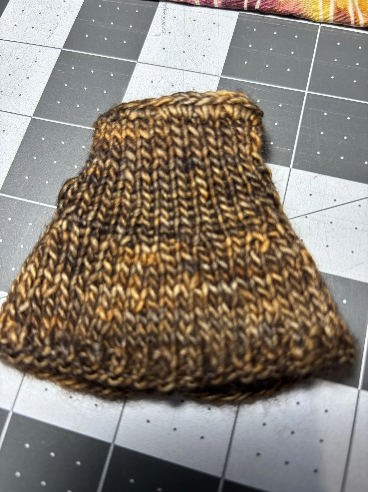 A close-up of a warm brown hand-knit doll dress showing the marled yarn and stitch texture.