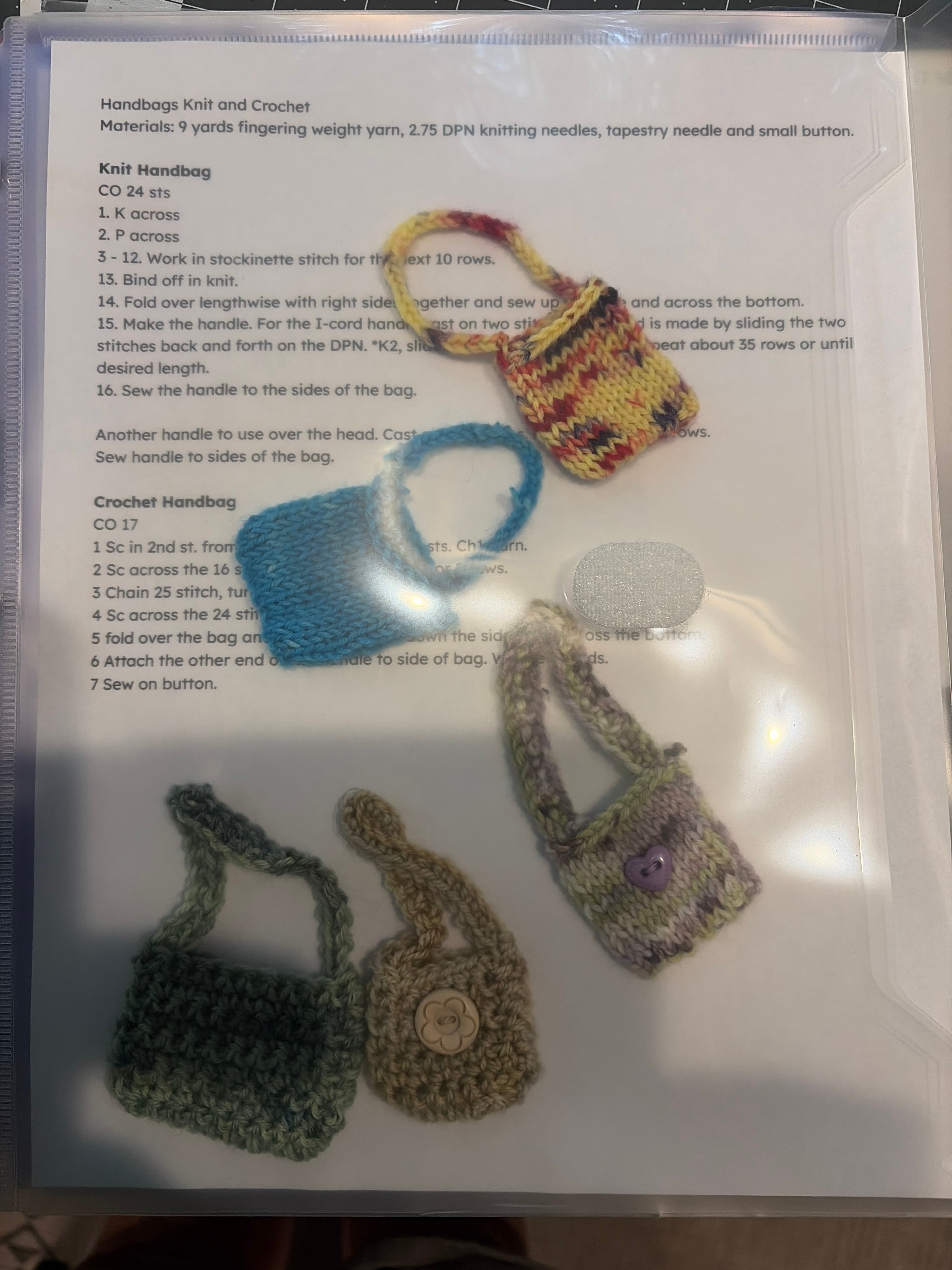 Four miniature doll handbags in red, blue, lilac and green with i-cord handles, on the handbag pattern sheet.