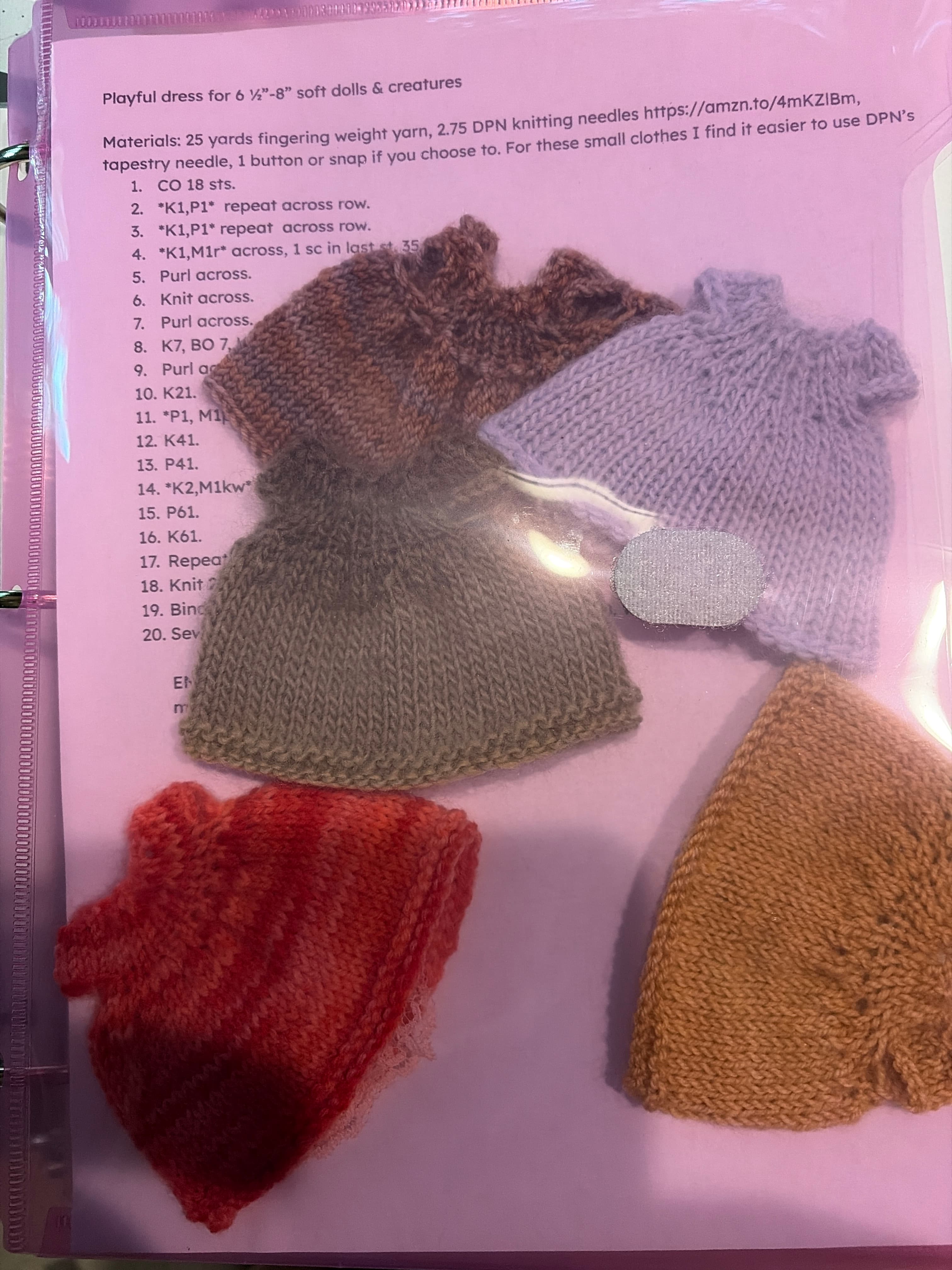 Several knit doll dresses in lilac, sage, brown and coral arranged on the playful dress pattern sheet.