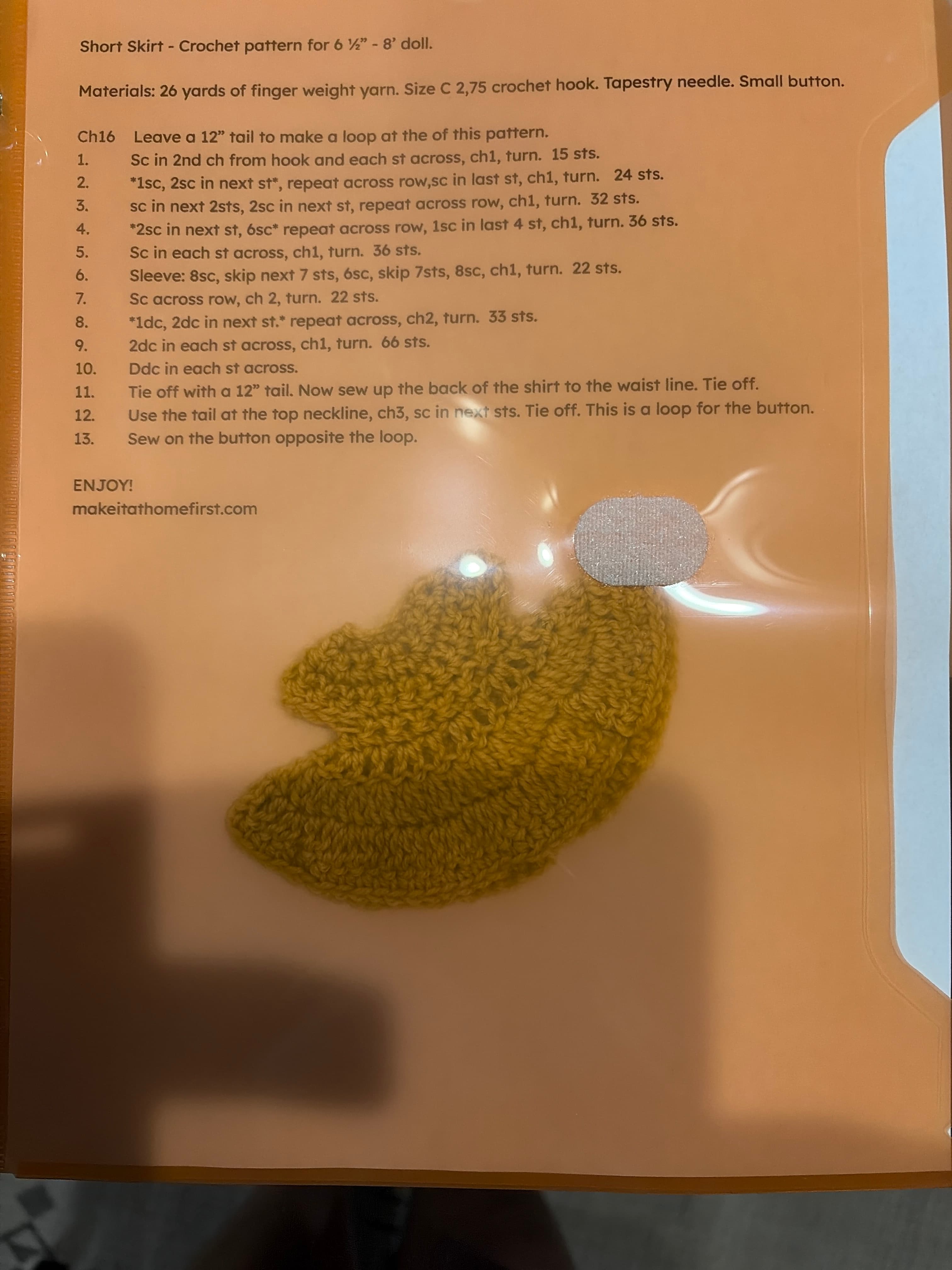 A mustard crochet doll skirt resting on its written crochet pattern.